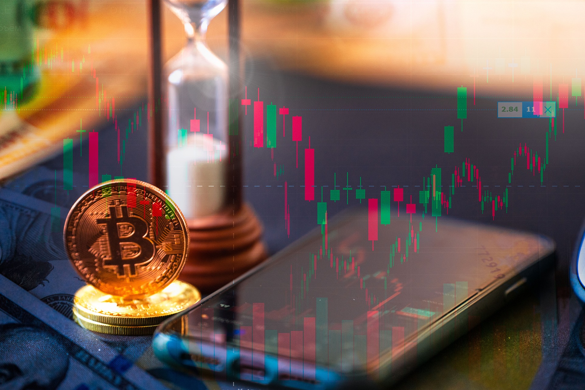 A gold coin and an hourglass in front of a phone displaying candlestick charts