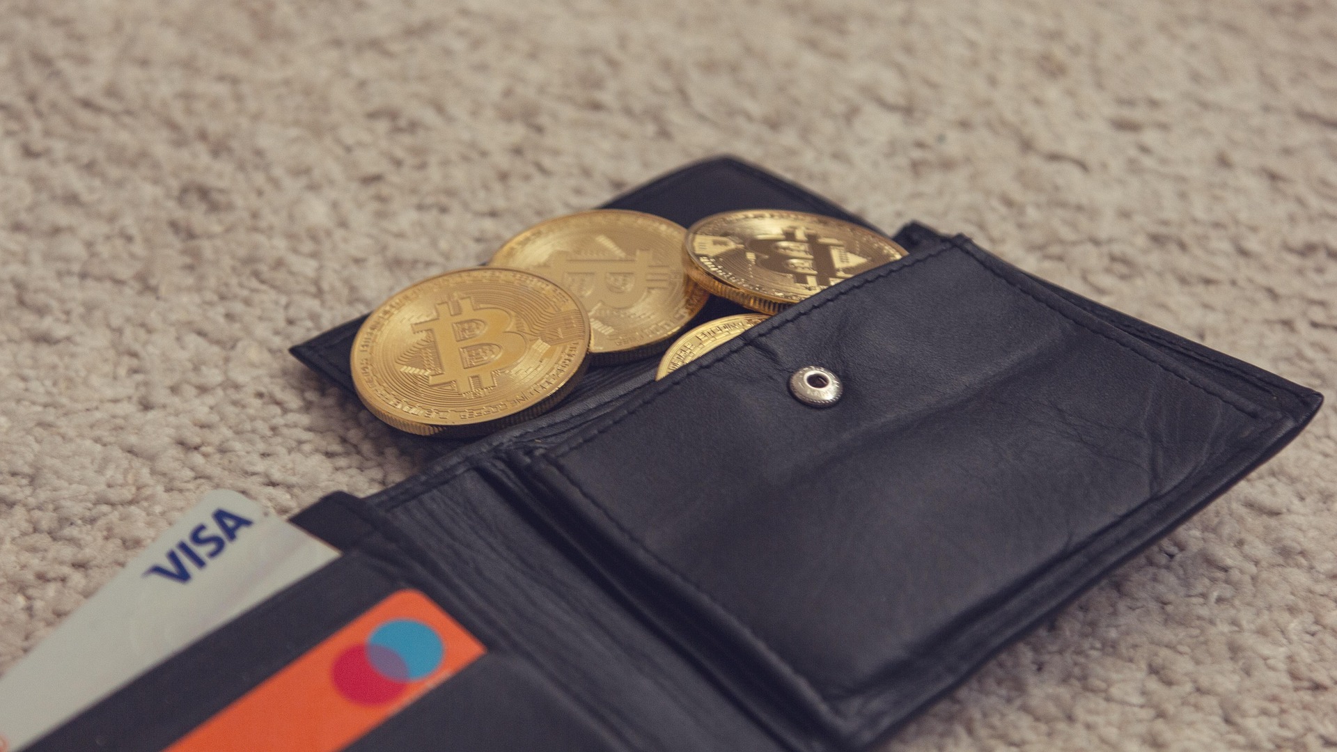 A leather wallet holding gold coins alongside payment cards on a carpet